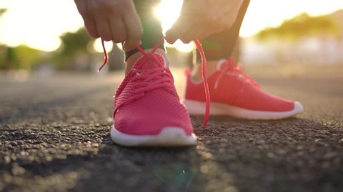 Close up of woman tying shoe laces and running along the palm avenue at sunset. Slow motion
