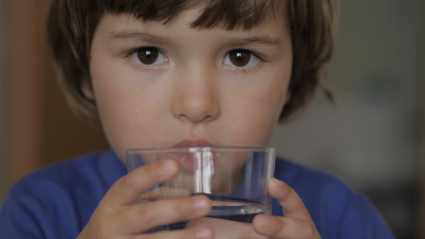 Cute child boy drinking a glass water at home. Slow motion of little boy drinking water. Closeup. Child drinking a cup water with of lemon - healthy body care.