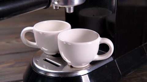 coffee is poured from a coffee machine into two cups