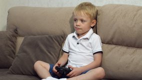 Cute boy playing video games at home. Cheerful boy sitting on a sofa and playing video games. Slow motion. High resolution.