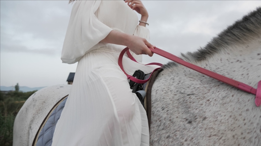pretty lady in long white dress sits in saddle holding halter handsome man walks near horse low angle shot slow motion