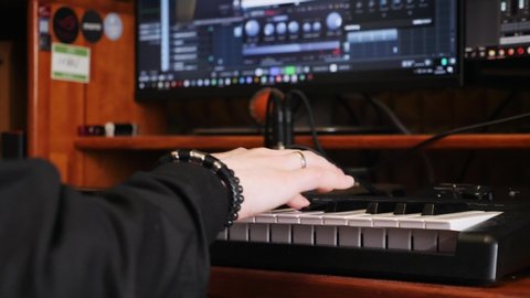 Young artist composing a song on electronic piano keyboard at home recording studio. Hand playing on piano in music studio. Sound engineer working on producing a song.