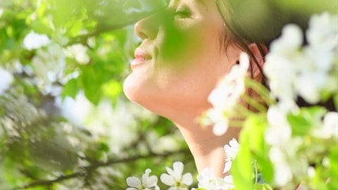 Beauty young woman enjoying nature in spring apple orchard, Happy Beautiful girl in Garden with blooming trees. Beauty model girl face. Smiling Person smelling blossom flowers 4K UHD video 3840X2160