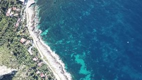 Drone flying over the rocky seashore near Sferracavallo village, Palermo province, Sicily, Italy, with waves dashing on the rocks and seabed clearly visible through the transparent waters