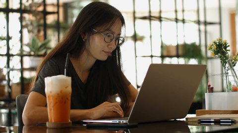 Asian Woman Works on a Laptop while Sitting in Cafe.