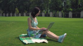 Businesswoman sitting on the lawn working on computer. Happy young professional woman surfing internet chatting with clients or has online video call with partner in the park. Female works remote on