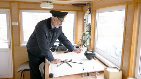 Planning a long trip on a cruise ship. Elderly grey-haired captain of the ship is plotting the navigation route on the map in the wheelhouse.