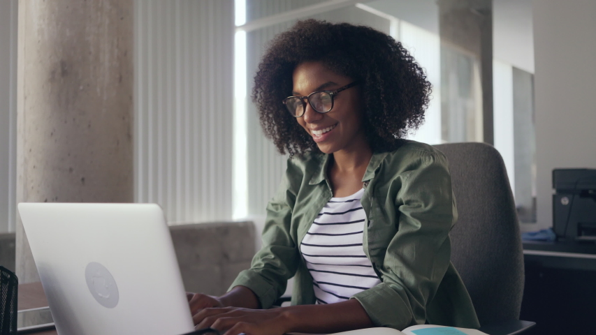Young woman sitting at desk in front of laptop stretching her arms