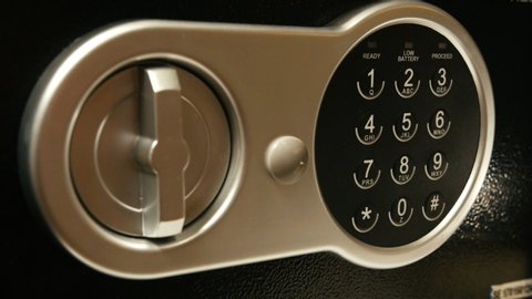 Close-up shot of a black safe being opened by a hand entering the correct pin and afterwards turning the latch to reveal it's content.