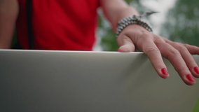 Detail shot of woman's hand with red nails opening the laptop in the park with defocused background. Clip represents feminity, independence, women entrepreneurship and leadership.
