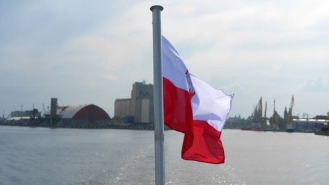 Flag of Poland waving on flag pole of ship, port of Szczecin in background