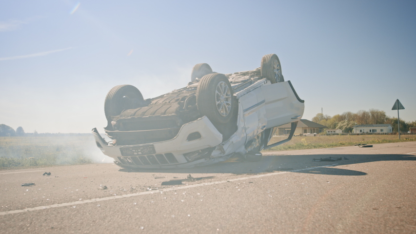 Horrific Traffic Accident, Rollover Smoking and Burning Vehicle Lying on its Roof in the Middle of the Road after Collision. Daytime Crash Scene with Severely Damaged Car. Royalty-Free Stock Footage #1032835862