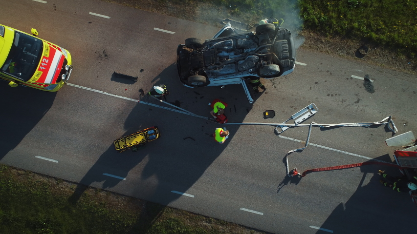 Aerial View: Rescue Team of Firefighters and Paramedics Work on a Car Crash Traffic Accident Scene. Preparing Equipment, First Aid Help. Saving Injured and Trapped People from the Vehicle. Zoom in