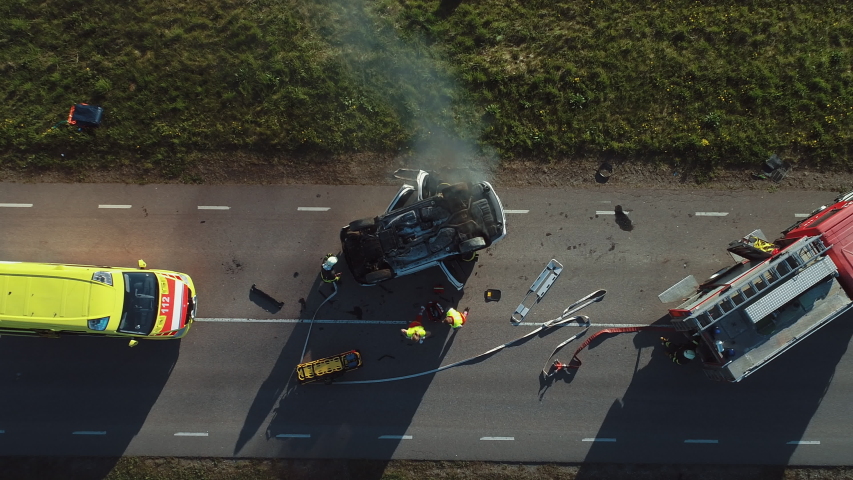 Aerial View: Rescue Team of Firefighters and Paramedics Work on a Car Crash Traffic Accident Scene. Preparing Equipment, First Aid Help. Saving Injured and Trapped People from the Burning Vehicle Royalty-Free Stock Footage #1032835907