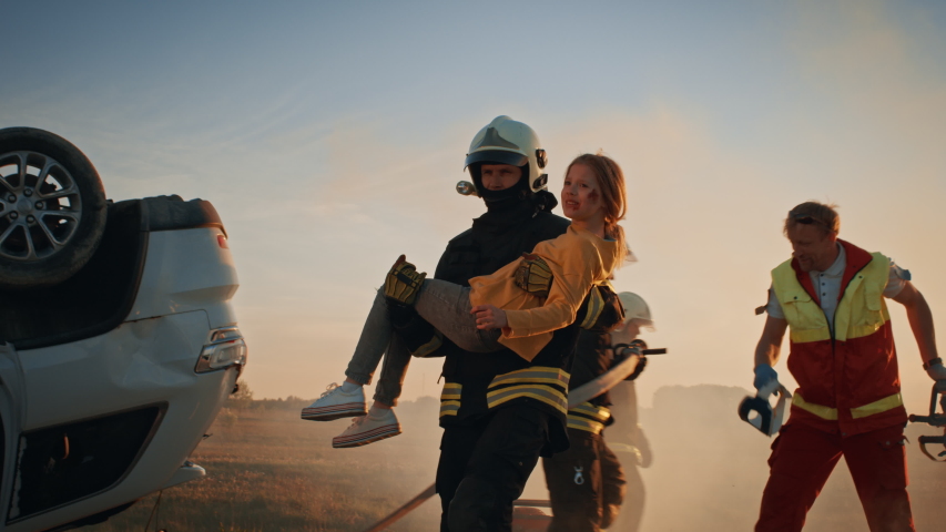 Brave Firefighter Carries Injured Young Girl to Safety where She Reunited with Her Loving Mother. In the Background Car Crash Traffic Accident Courageous Paramedics and Firemen Save Lives Royalty-Free Stock Footage #1032835931