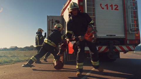 Rescue Team of Firefighters Arrive at the Crash, Catastrophe, Fire Site on their Fire Engine. Firemen Grab their Equipment, Prepare Fire Hoses and Gear from Fire Truck, Rush to Help Injured People
