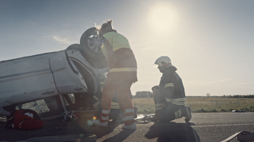 Car Crash Traffic Accident: Paramedics and Firefighters Plan Rescuing Passengers Trapped in a Rollover Vehicle. Medics Prepare First Aid Equipment, Firemen Use Hydraulic Cutters Spreader Royalty-Free Stock Footage #1032836258