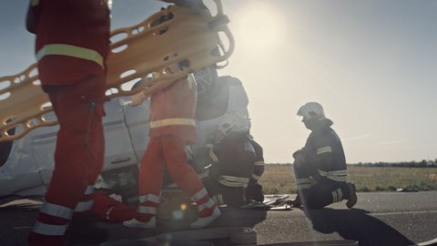 Car Crash Traffic Accident: Paramedics and Firefighters Plan Rescuing Passengers Trapped in a Rollover Vehicle. Medics Prepare First Aid Equipment, Firemen Use Hydraulic Cutters Spreader