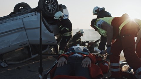 On the Car Crash Traffic Accident Scene: Paramedics Giving First Aid Oxygen Mask to Female Victim of the Accident. Firefighters Extinguish Fire and Use Hydraulic Cutter to Free Other Passengers