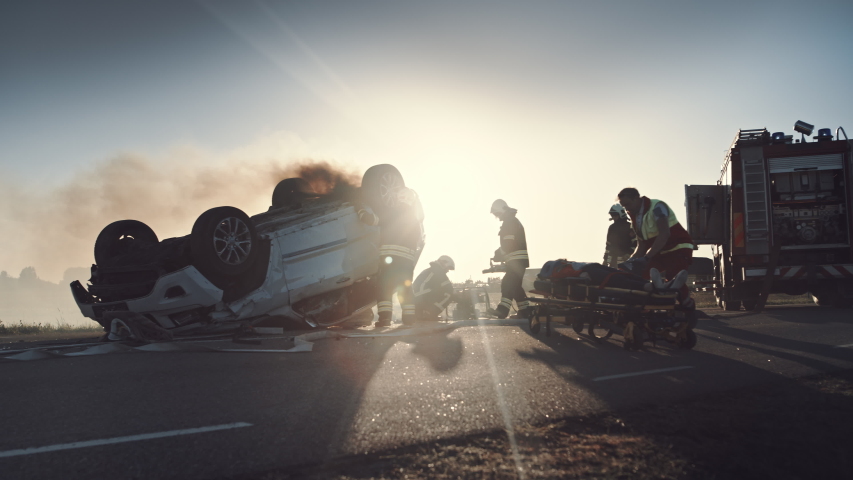 On the Car Crash Traffic Accident Scene: Paramedics Giving First Aid Oxygen Mask to Female Victim of the Accident. Firefighters Extinguish Fire and Use Hydraulic Cutter to Free Other Passengers Royalty-Free Stock Footage #1032836264