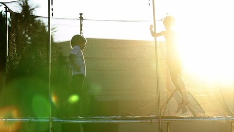 Kids jumping and bouncing inside trampoline outdoors in the sunlight flare.