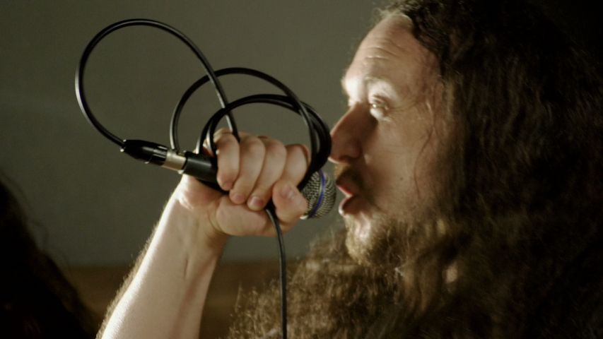 Musical metal band. Man singing a song into microphone, having performance with rock band in studio. 4K