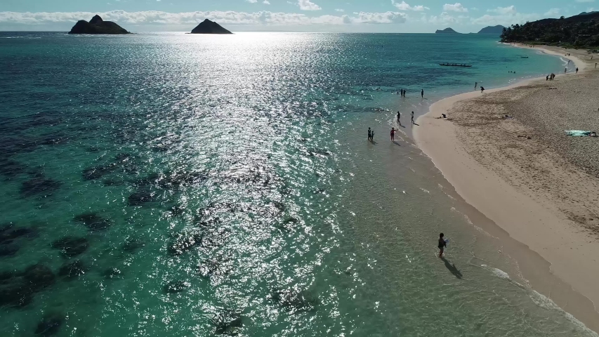Aerial view of Lanikai beach, Honolulu, Hawaii, low angle view with drone camera moving forward, sun reflection with shore and backlit island in the background, color graded
