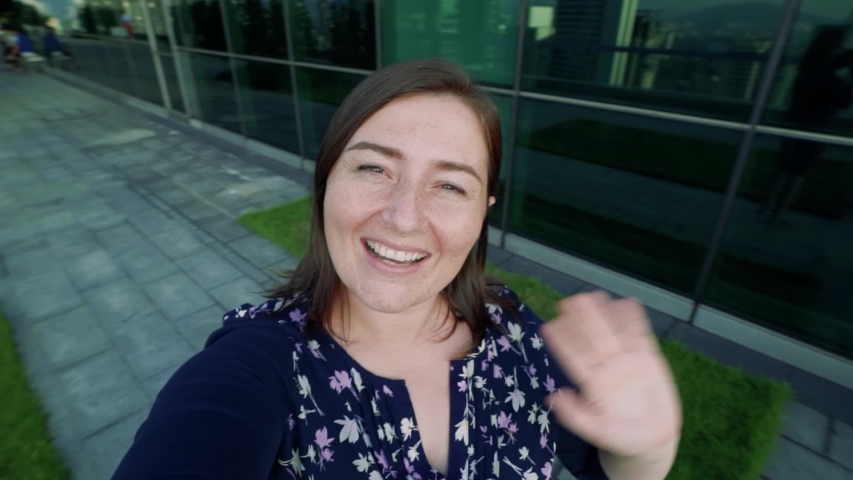 Cheerful freckled girl have online video chat talking and standing on high floor of high-rise building in modern city. POV