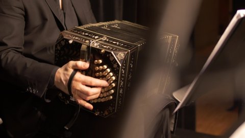 A Bandoneon accordion player is practicing for a tango music show, while a music stand is blurred in the foreground.