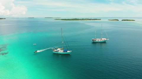 Aerial orbital panorama around two yachts as a raft speeds to a nearby island