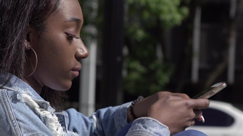 African American teen girl texting while sitting in sunshine 4k