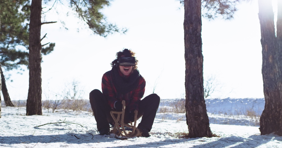 Attractive guy with a large smile in front of the camera using a virtual reality glasses outside on the winter time using a sleigh he have a good adventure