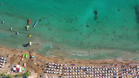 Aerial view of Coral Bay beach with umbrellas, swimming people in transparent sea water. Pegeia, Paphos District, Cyprus