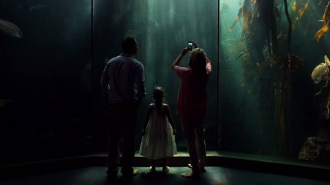 Happy family looking at fish and taking pictures at the aquarium