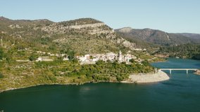 Side aerial panning video of a Spanish village on top of a hill by the lake on a sunny summer day, 4k drone footage