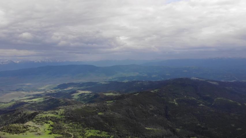 High altitude drone of green hills, pine trees and mountains in the background