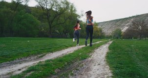 Amazing video capturing of a two sporty ladies running through of a beautiful mountain view with a green field ,in a perfect summer day