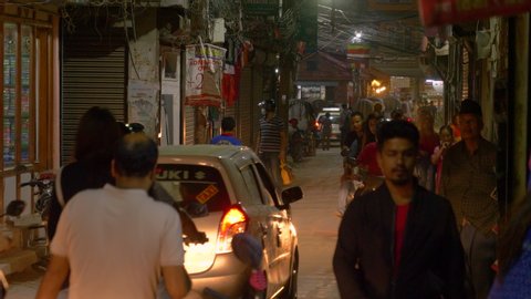 KATHMANDU, NEPAL - SEPTEMBER 2018: CLOSE UP: Pedestrians share the bumpy road with cars and motorbikes on a busy night in Kathmandu. Scenic view of busting streets full of traffic and travelers.
