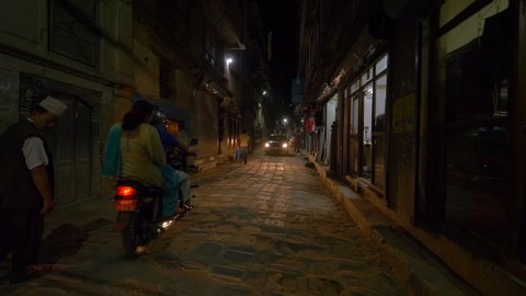 KATHMANDU, NEPAL - SEPTEMBER 2018: SLOW MOTION: Travelers in cars and on motorbikes exploring the dark city streets and driving past tourist shops in Kathmandu. Third world country city life at night.
