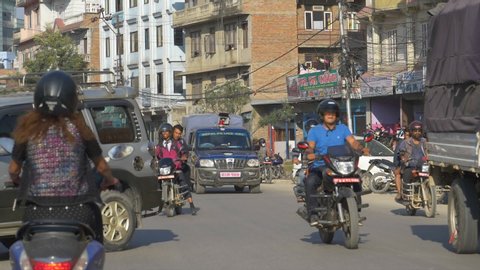KATHMANDU, NEPAL - SEPTEMBER 2018: SLOW MOTION: Local people riding motorbikes and driving old cars in downtown Kathmandu. Vehicles fill up the streets and pollute the air of a city in sunny Nepal.