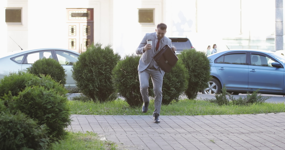 Attractive man with a beard and briefcase dancing in the street. Businessman or lawyer celebrates a good deal having fun in the city.