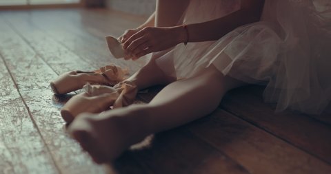Pointe shoes are dressed on legs, ballerina tying ribbons. Close-up.