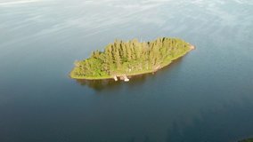 Aerial view over an isolated island. Drone fly forward a small island. Beautiful deep blue colour of the sea. Sunny summer morning. Cabins and boats along the shore.