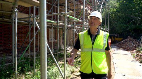 Male builder foreman construction worker on building site inspecting and checking scaffolding for health and safety