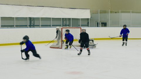 Panning shot of boys playing professional hockey on ice arena and attack the goal post but wide of goal