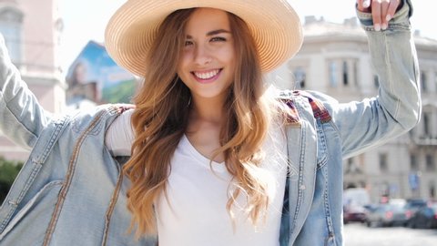 Attractive Girl Charming Smiles to the Camera in Slow Motion. Walking in big Park in Stylish Casual Clothes. Wears Straw Hat. Girl smiles sincerely, enjoy Sunny Day. Holidays. Smiles