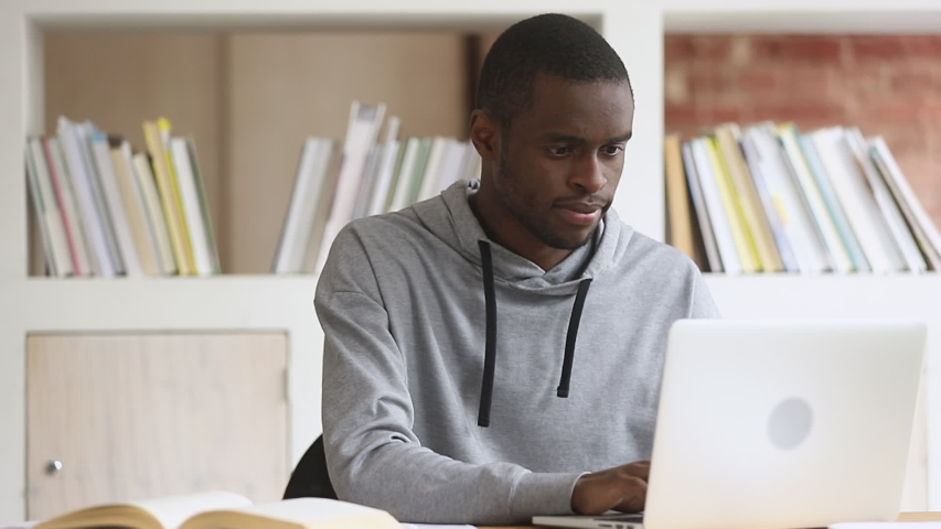 Focused african black male student using laptop search information internet course study online e learning in app typing on computer make notes write essay prepare for test exam sit at library desk Royalty-Free Stock Footage #1032911054