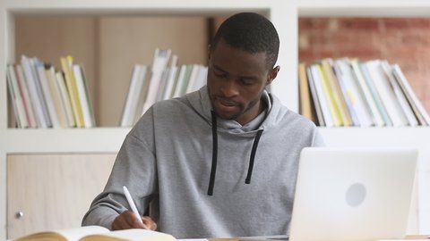 Focused african black male student using laptop search information internet course study online e learning in app typing on computer make notes write essay prepare for test exam sit at library desk