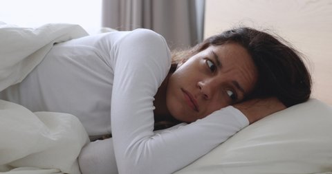 Frustrated upset young woman lying awake in bed alone trying to sleep suffer from insomnia or uncomfortable bad mattress, annoyed stressed lady insomniac feeling disturbed toss and turn in bedroom