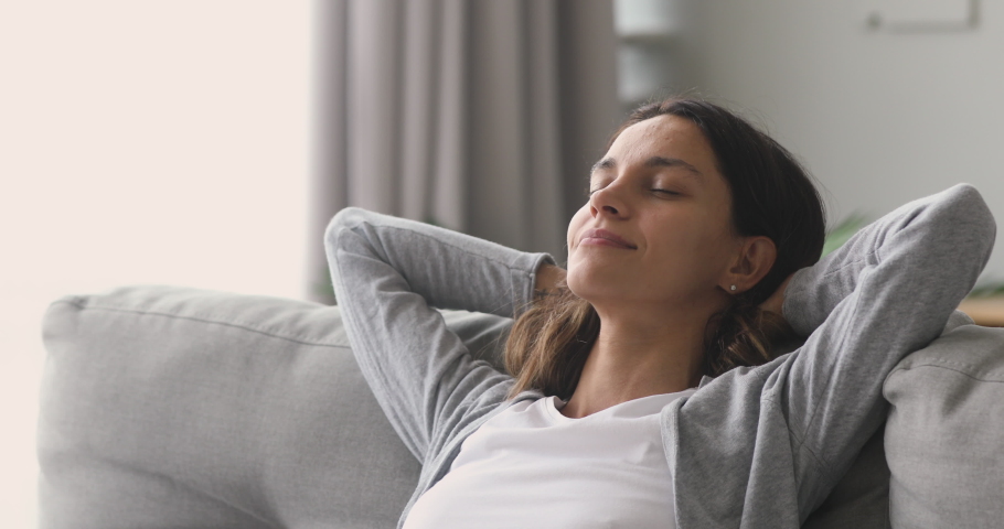 Happy relaxed young woman rest lounge lean on couch enjoy peaceful mood, healthy lazy calm girl dreaming breathing fresh air sit on comfortable sofa in living room on stress free cozy day at home | Shutterstock HD Video #1032911126